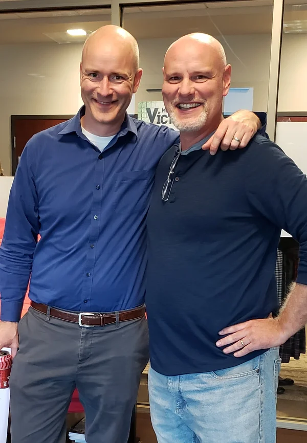 Miss Elisa’s husband and Jim Wooldridge (Señor Wooly) posing together, arms around each other — both bald, both grinning
